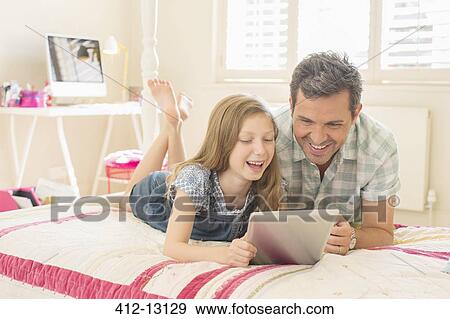 Stock Photo - Father and daughter using digital tablet on bed. Fotosearch