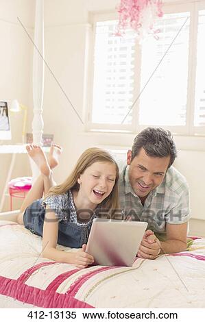 Stock Photography - Father and daughter using digital tablet on bed. Fotosearch