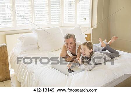 Father and daughter using laptop on bed View Large Photo Image Stock Photo - Father and daughter using laptop on bed. Fotosearch