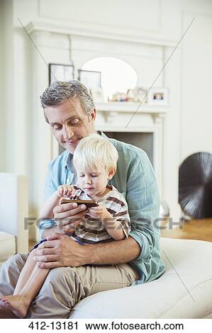 Father and son using cell phone in living room View Large Photo Image Stock Image - Father and son using cell phone in living room. Fotosearch