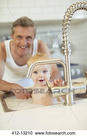 Stock Image - Father bathing baby in kitchen sink. Fotosearch