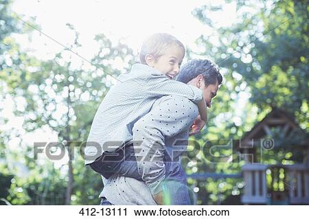 Stock Image - Father carrying son piggyback outdoors. Fotosearch