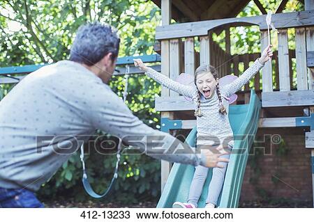 Stock Image - Father catching daughter on slide. Fotosearch
