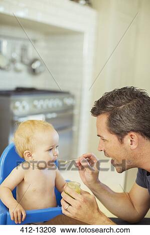 Stock Photo - Father feeding baby in high chair. Fotosearch