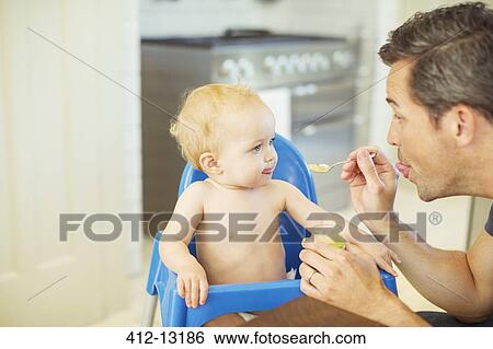 Father feeding baby in high chair View Large Photo Image Stock Photograph - Father feeding baby in high chair. Fotosearch
