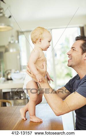 Stock Photo - Father helping baby walk on table. Fotosearch