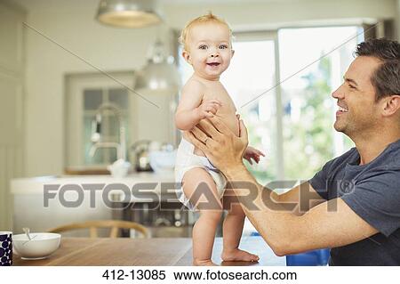 Stock Photography - Father helping baby walk on table. Fotosearch