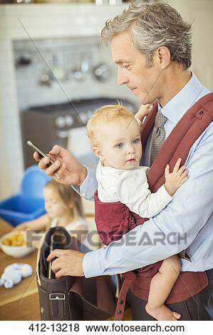 Stock Photo - Father holding baby and checking cell phone. Fotosearch