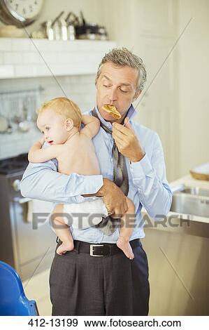 Father holding baby and eating breakfast View Large Photo Image Stock Photo - Father holding baby and eating breakfast. Fotosearch