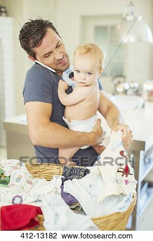 Father holding baby and folding laundry while talking on cell phone View Large Photo Image Stock Image - Father holding baby and folding laundry while talking on cell phone. Fotosearch