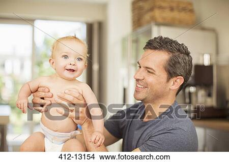 Picture - Father holding baby in kitchen. Fotosearch