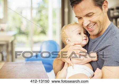 Stock Image - Father holding baby in kitchen. Fotosearch