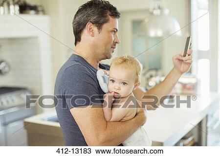 Father using cell phone and holding baby View Large Photo Image Stock Image - Father using cell phone and holding baby. Fotosearch