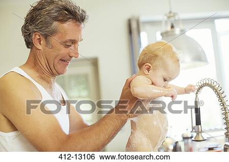 Stock Photograph - Father washing baby in kitchen sink. Fotosearch