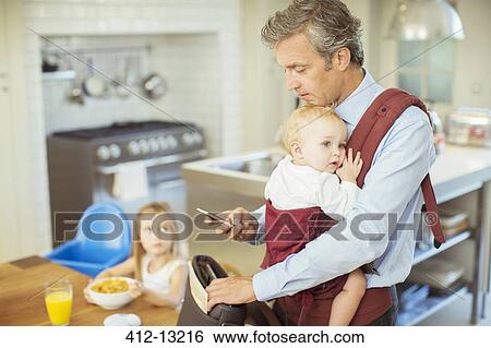 Stock Photograph - Father with baby packing bag for work. Fotosearch