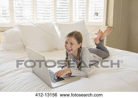 Stock Photograph - Girl using laptop on bed. Fotosearch