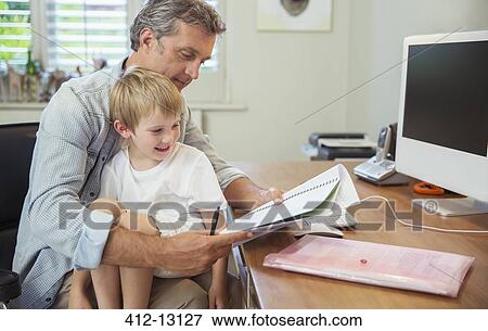 Stock Photo - Son sitting on working father's lap. Fotosearch