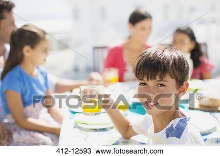Stock Image - Boy drinking juice at table on sunny patio. Fotosearch
