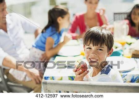 Boy eating fruit with family at table on sunny patio View Large Photo Image Stock Photo - Boy eating fruit with family at table on sunny patio. Fotosearch