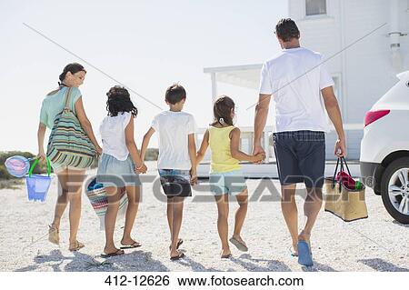 Stock Photograph - Family holding hands and carrying beach gear in sunny driveway. Fotosearch