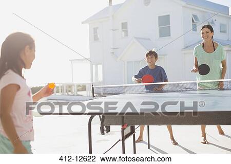 Stock Image - Family playing table tennis together outside house. Fotosearch