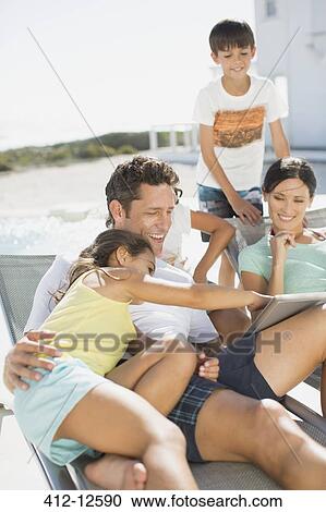 Family using digital tablet on lounge chairs at poolside View Large Photo Image Stock Image - Family using digital tablet on lounge chairs at poolside. Fotosearch