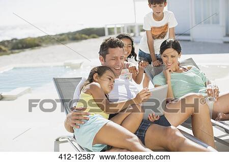Stock Photo - Family using digital tablet on lounge chair at poolside. Fotosearch