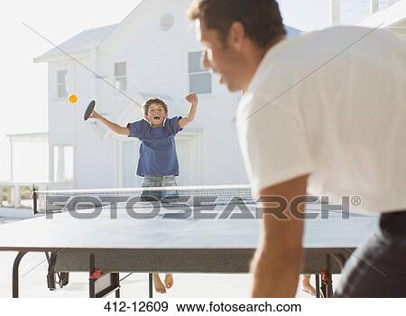 Stock Photo - Father and son playing table tennis outdoors. Fotosearch