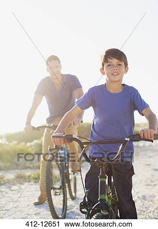 Stock Image - Father and son riding bicycles on sunny beach. Fotosearch