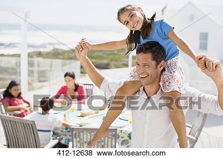 Stock Photo - Father carrying daughter on shoulders on sunny patio. Fotosearch