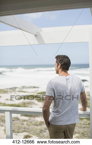 Stock Photograph - Man looking at ocean view from balcony. Fotosearch