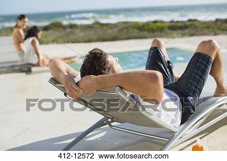 Man relaxing in lounge chair at poolside View Large Photo Image Stock Image - Man relaxing in lounge chair at poolside. Fotosearch
