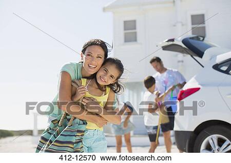 Stock Image - Mother and daughter hugging outside beach house. Fotosearch