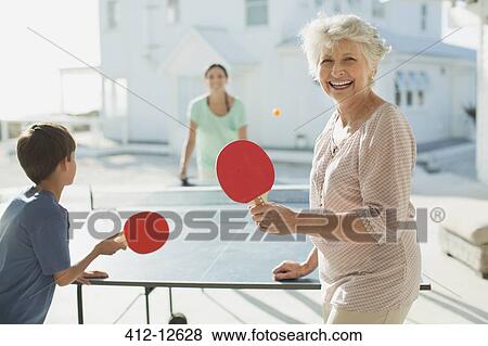 Stock Photo - Multi-generation family playing table tennis outside beach house. Fotosearch