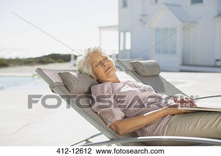 Stock Image - Senior woman sleeping on lounge chair at poolside. Fotosearch