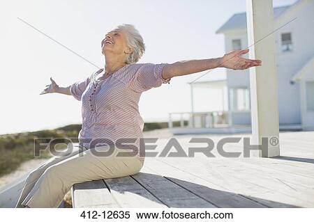 Senior woman with arms outstretched on sunny deck View Large Photo Image Stock Photography - Senior woman with arms outstretched on sunny deck. Fotosearch