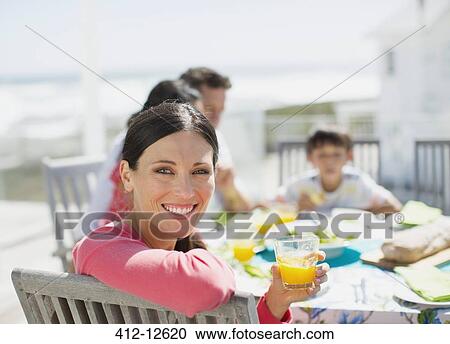 Woman drinking orange juice at table on sunny patio View Large Photo Image Stock Image - Woman drinking orange juice at table on sunny patio. Fotosearch