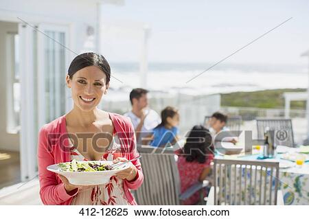 Stock Photography - Woman holding salad bowl on sunny patio overlooking ocean. Fotosearch