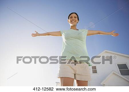Stock Image - Woman smiling with arms outstretched against blue sky. Fotosearch