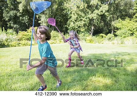 Stock Image - Boy and girl running with butterfly nets in grass. Fotosearch