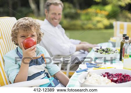 Stock Photo - Boy playing with food at table in backyard. Fotosearch