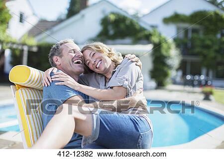 Stock Image - Couple relaxing in lounge chair at poolside. Fotosearch