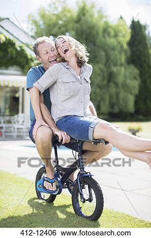 Couple riding small bicycle in grass View Large Photo Image Stock Photograph - Couple riding small bicycle in grass. Fotosearch