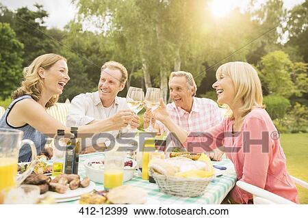 Couples toasting wine glasses at table in backyard View Large Photo Image Stock Photo - Couples toasting wine glasses at table in backyard. Fotosearch