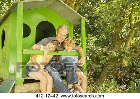 Stock Image - Father and children relaxing together in treehouse. Fotosearch