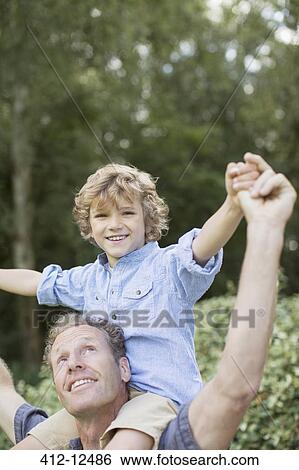 Stock Photograph - Father carrying son on shoulders outdoors. Fotosearch