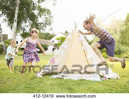 Stock Photo - Father chasing children around teepee in backyard. Fotosearch