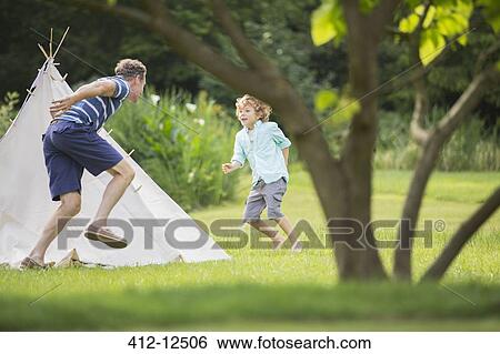 Stock Photograph - Father chasing son around teepee in backyard. Fotosearch