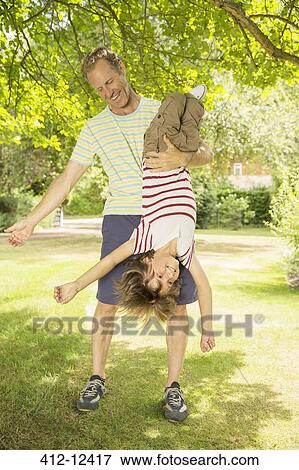 Stock Photo - Father holding son upside-down in backyard. Fotosearch