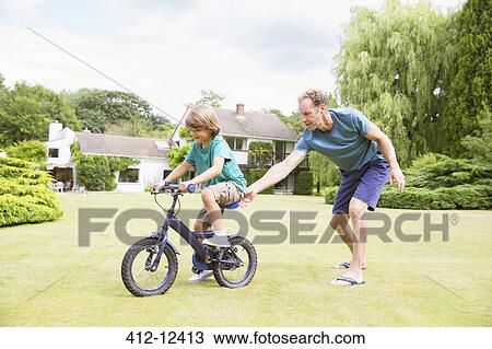 Father pushing son on bicycle in backyard View Large Photo Image Stock Image - Father pushing son on bicycle in backyard. Fotosearch